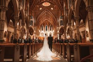 bride walking down the aisle with her dad. Photo from behind with a large cathedral ceiling in front of them. Holy name Cathedral in Chicago.