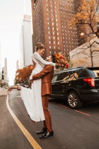 Groom in brown suit picking up his bride in the middle of Michigan avenue in Chicago