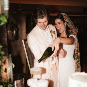 Bride and groom, high energy, photo pouring champagne into a champagne tower. groom has peach suit and bride has floral veil